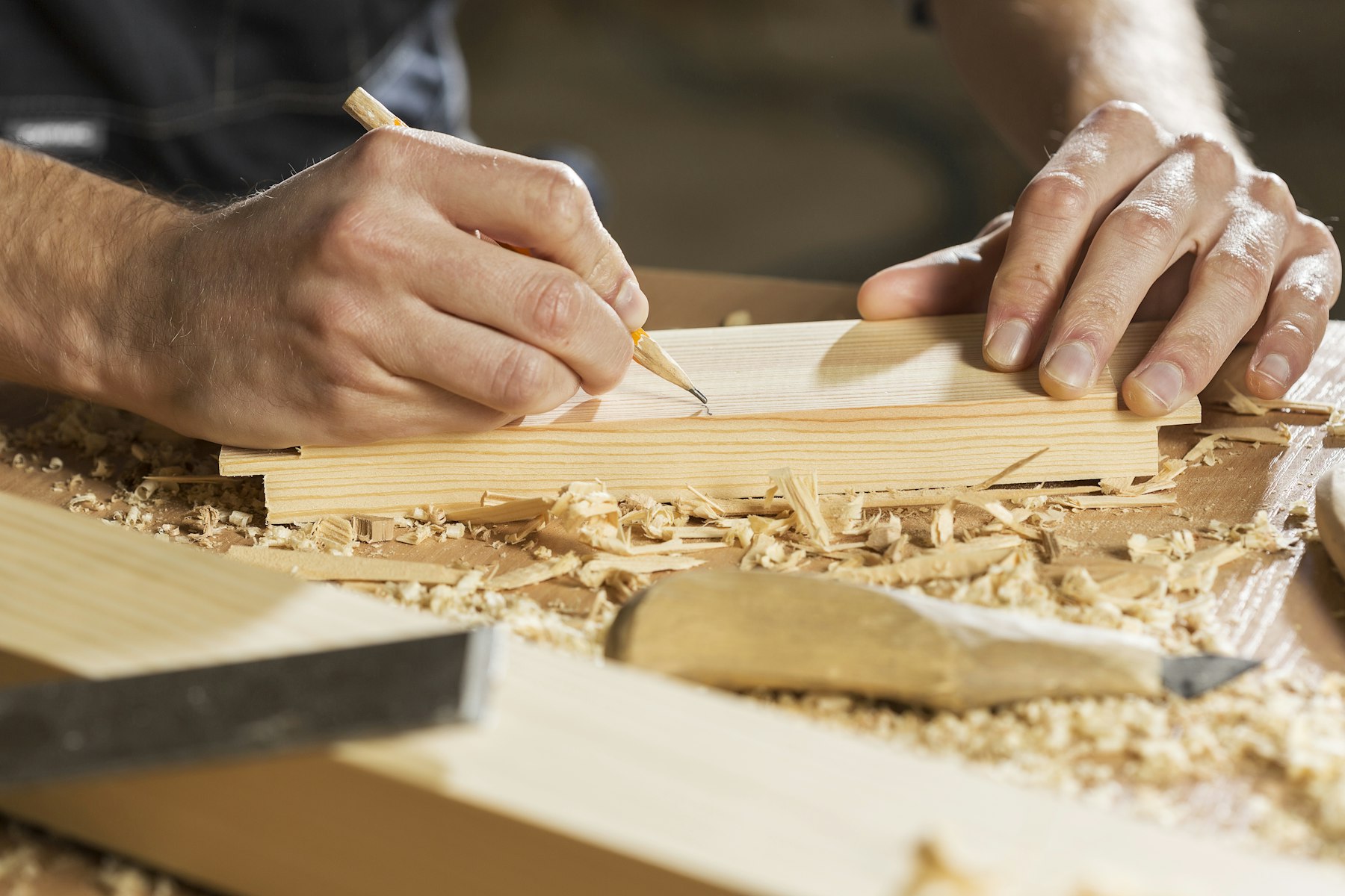 Hands marking a cut line on pine with a pencil, surrounded by shavings