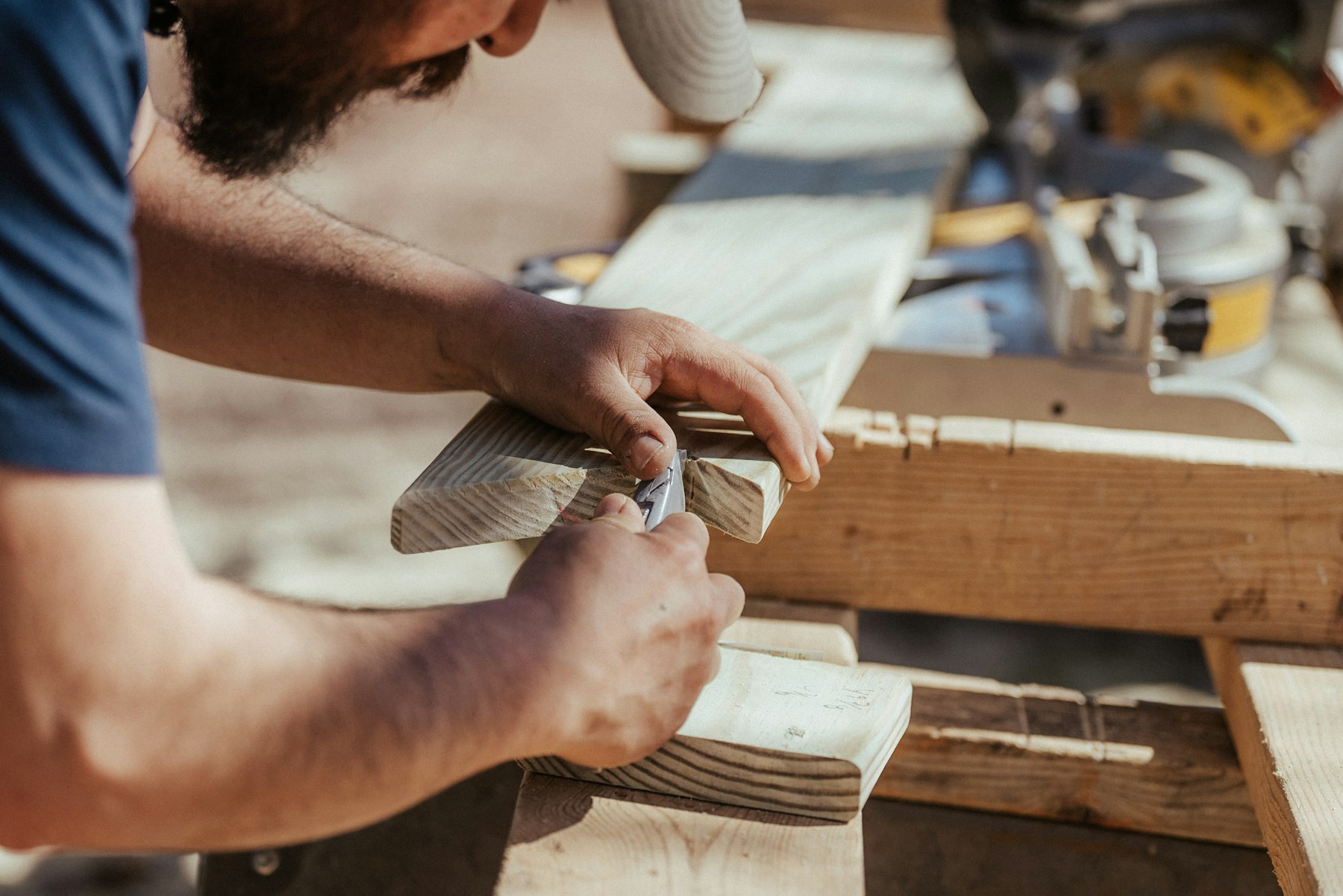 Hands trimming a notch in a timber board beside a mitre saw