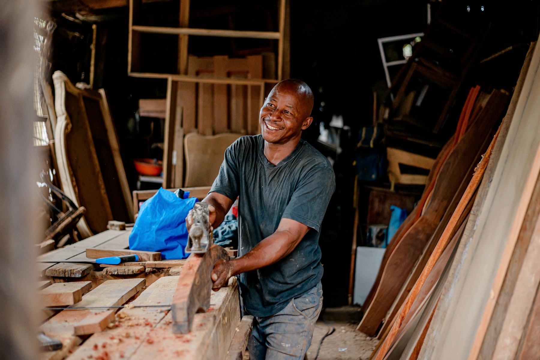 A smiling carpenter planing a length of timber at a workbench