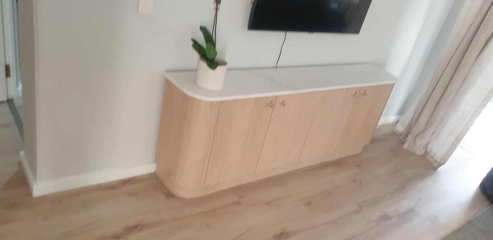Long low TV unit in pale oak with rounded ends and a white stone top