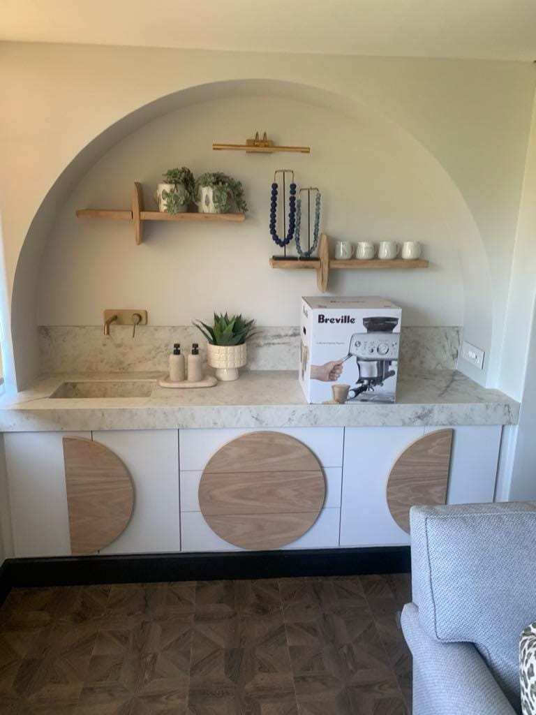 Coffee station in an arched alcove with white cabinets inlaid with oak circles