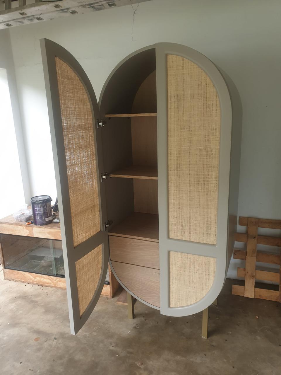 Tall arched cabinet with rattan door panels, open to show oak shelves and drawers